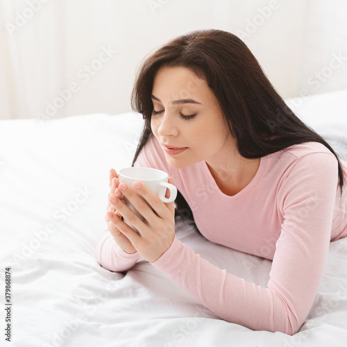 Millennial woman enjoying morning coffee in bed, free space