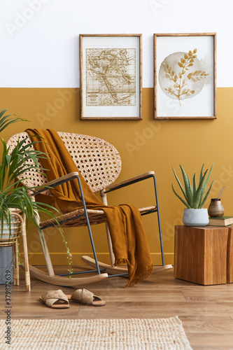 Stylish composition of living room interior with design rattan armchair, two mock up poster frames, plants, cube, palid and personal accessories in honey yellow home decor. Template. photo