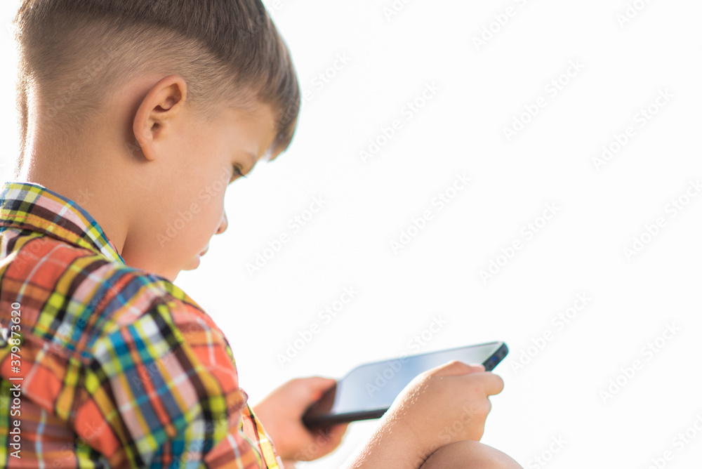 The child looks into the phone while sitting in the summer on the street. Little boy with a mobile in his hands. The child looks into the phone while sitting in the summer on the street. Little boy with a mobile in his hands.
