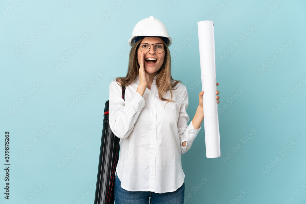 Slovak architect girl holding blueprints isolated on blue background shouting with mouth wide open Slovak architect girl holding blueprints isolated on blue background shouting with mouth wide open