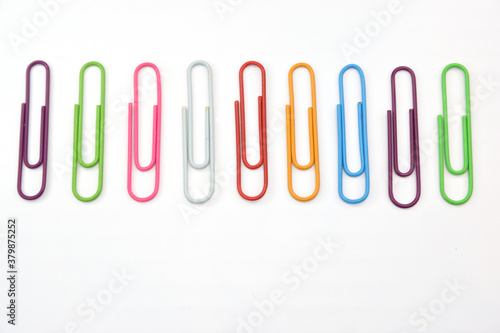Set of colored stationery paper clips laid out in a row on a white background.