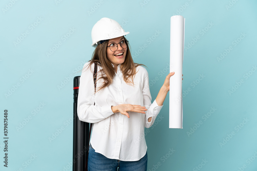 Slovak architect girl holding blueprints isolated on blue background with surprise expression while looking side Slovak architect girl holding blueprints isolated on blue background with surprise expression while looking side