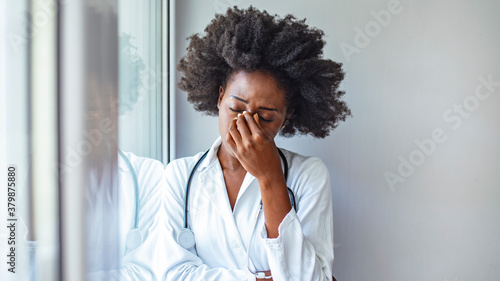 Depressed doctor. Tired doctor near window. Portrait of stressed doctor woman in office. Displeased black healthcare worker.  photo