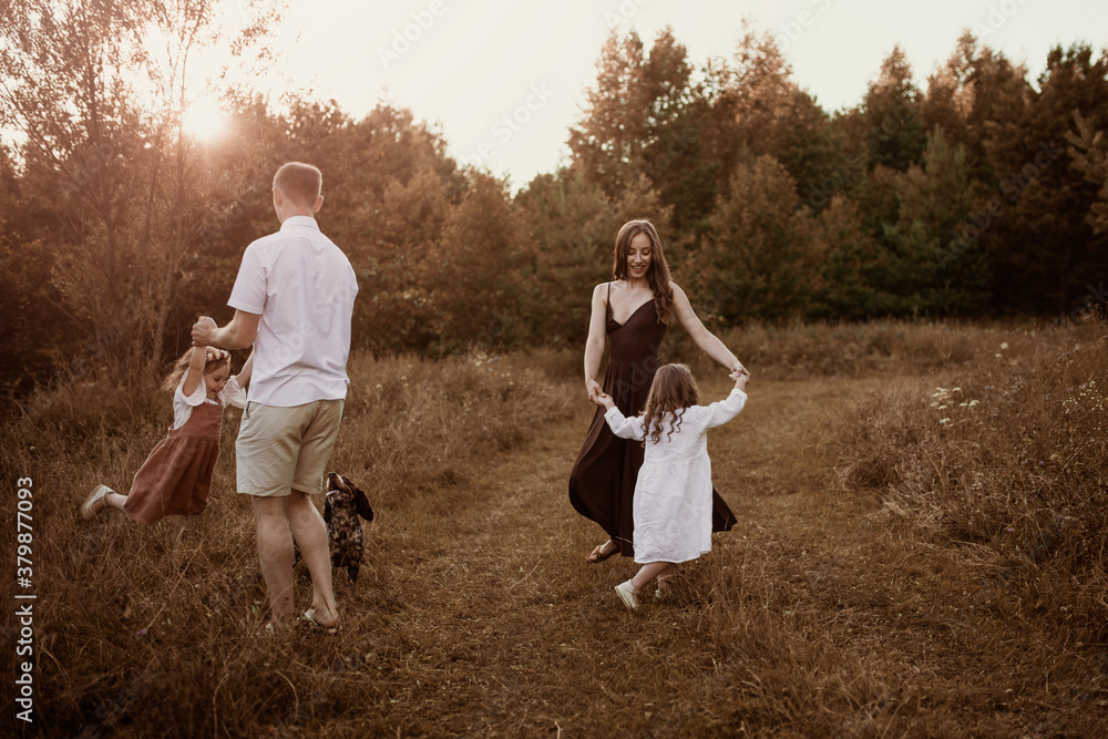 Cheerful young family with two children plays and dances in the field in summer, daughter with Down syndrome in a Caucasian family, lifestyle and brown toning. Candide childhood and parenting Cheerful young family with two children plays and dances in the field in summer, daughter with Down syndrome in a Caucasian family, lifestyle and brown toning. Candide childhood and parenting