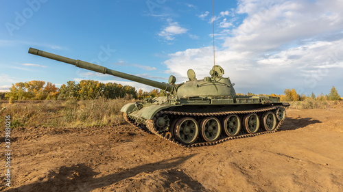 A side shot of old russian tank T-62 in the field. Blue cloudy sky as a background.