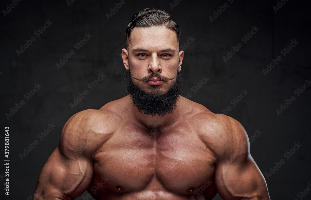 Handsome bearded bodybuilder with naked torso and with modern hairstyle posing in dark background.