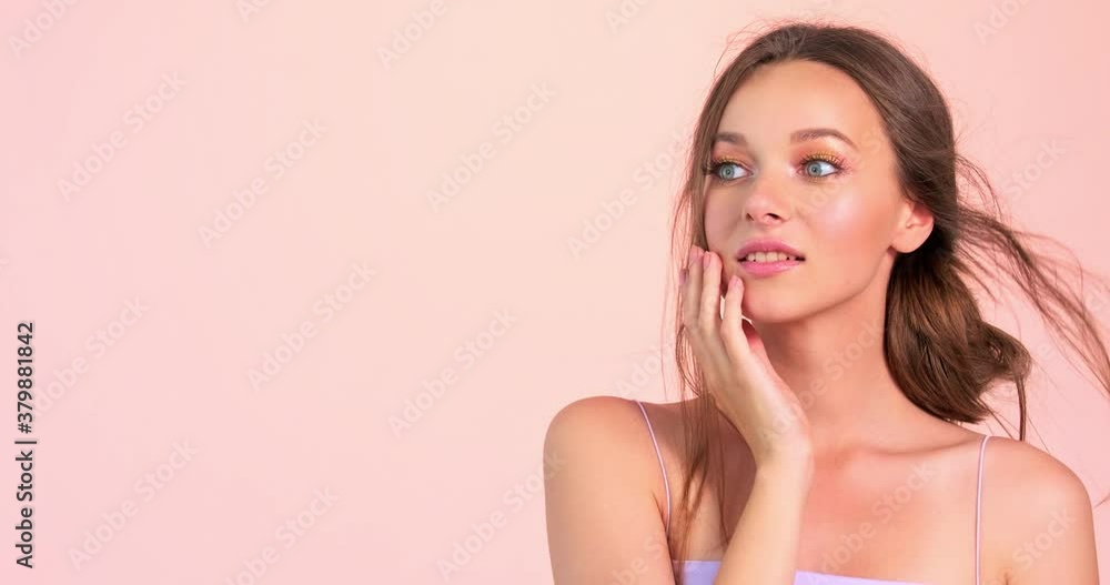 Young wondering woman puts her hand to her face over pink background. Surprised caucasian girl looking away. Happy young astonishment girl posing before camera. 4K. Young wondering woman puts her hand to her face over pink background. Surprised caucasian girl looking away. Happy young astonishment girl posing before camera. 4K.