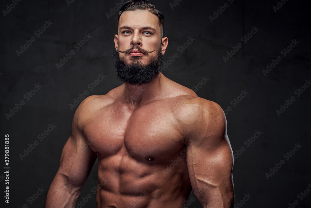 Strong naked guy with black beard and modern hairstyle posing in dark and gray background.