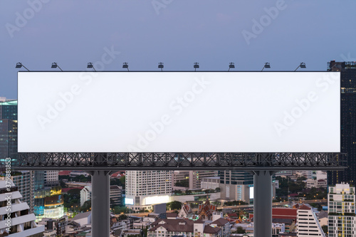 Blank white road billboard with Bangkok cityscape background at sunset. Street advertising poster, mock up, 3D rendering. Front view. The concept of marketing communication to promote or sell idea.