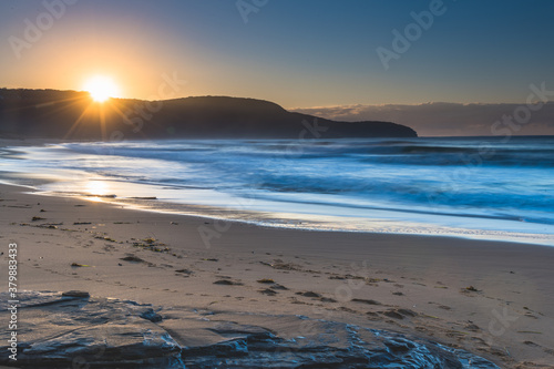 Clear skies winter sunrise seascape with sunburst over the headland