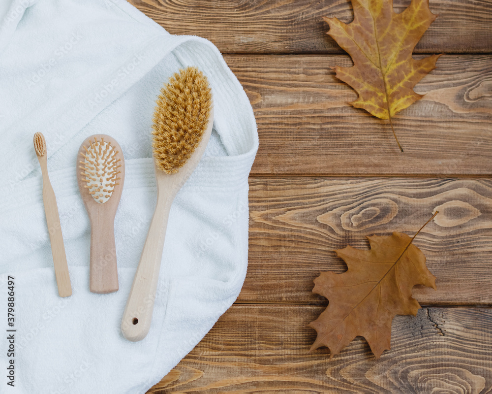 Wooden body brush, wooden comb, wooden toothbrush, bathrobe and autumn leaves on a wooden background. Place for text. Selective focus.
