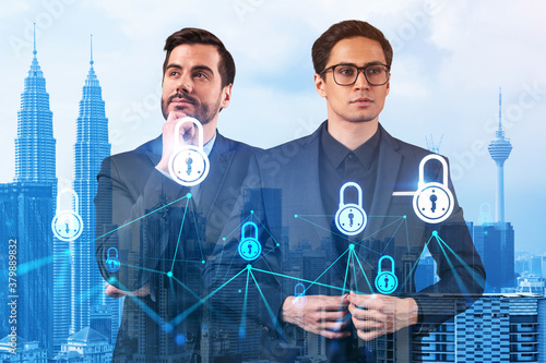 Two handsome businessman in suits thinking about career opportunities at cybersecurity compliance division to protect clients confidential information. IT lock icons over Kuala Lumpur background. photo