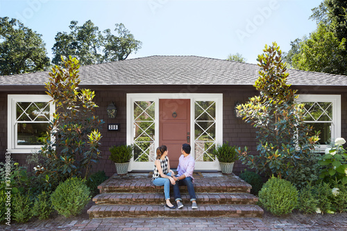 Young multiethnic couple sitting on the front steps looking back at their new home
