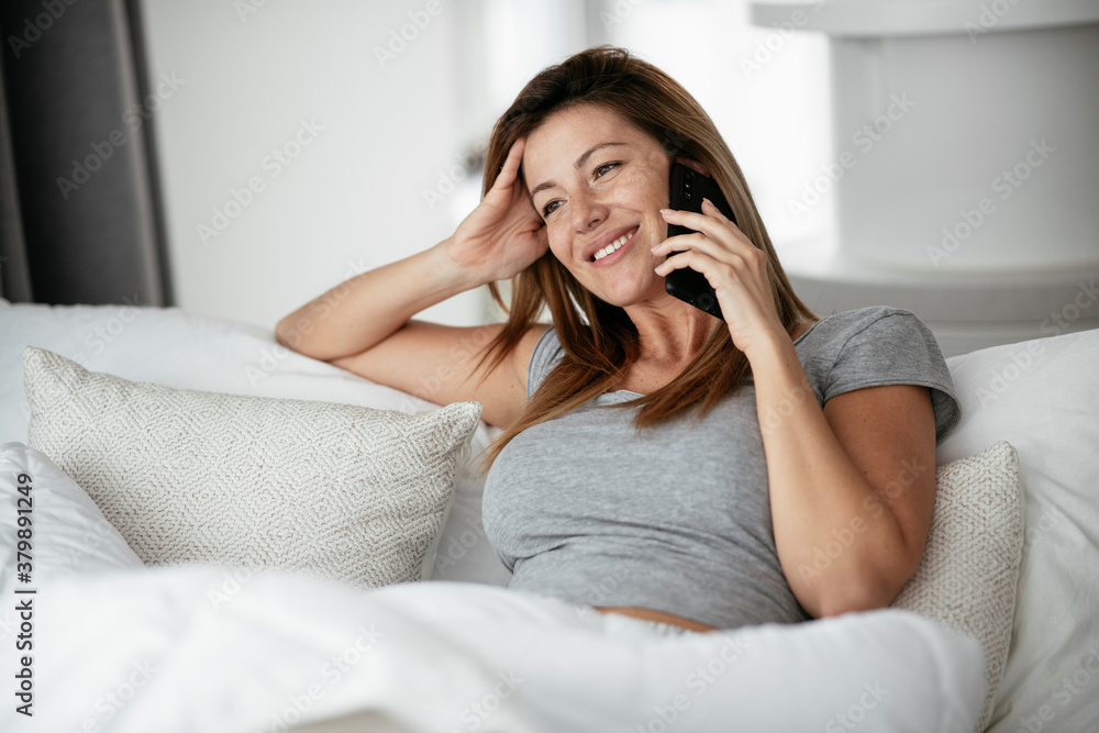 Young beautiful woman talking to the phone in bed. Girl lying on bed.. Young beautiful woman talking to the phone in bed. Girl lying on bed..