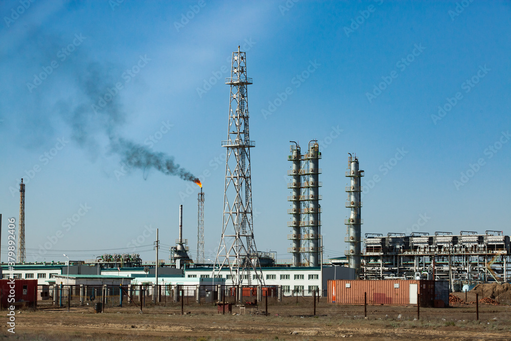 Oil refinery and gas processing plant. View of communication tower, refining columns, gas torch mast, pipelines and industrial building against clear  blue sky.