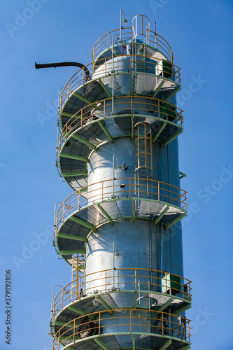 Close-up of grey metal distillation tower. Oil refining column on blue sky. Petrochemical plant.