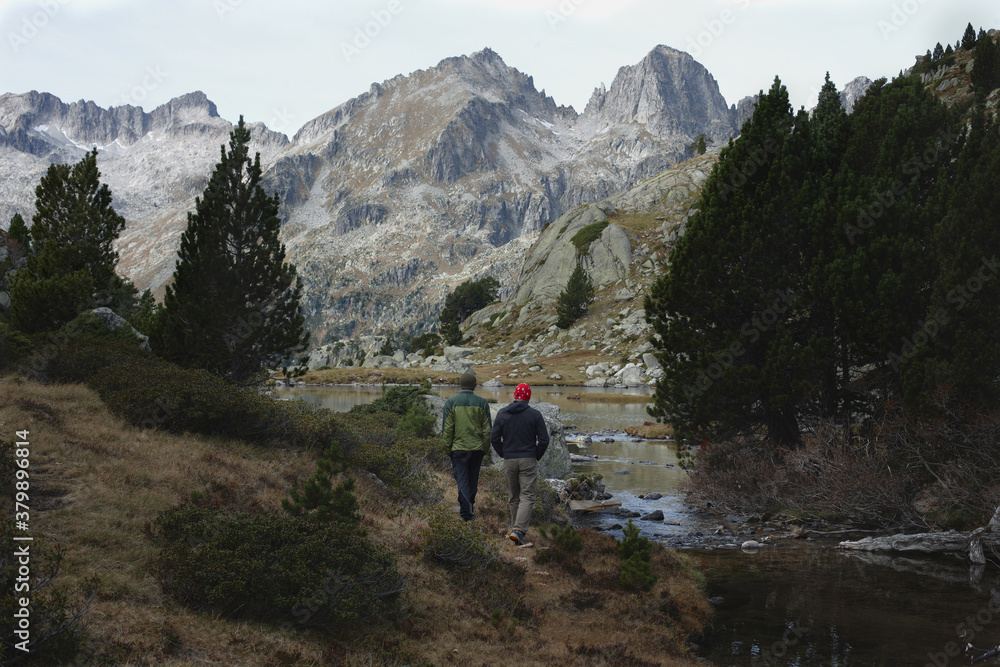 Two men hiking by the mountains and a lake in the Pyrenees Two men hiking by the mountains and a lake in the Pyrenees