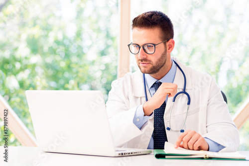 Male doctor sitting at desk and using laptop while working in doctor's office