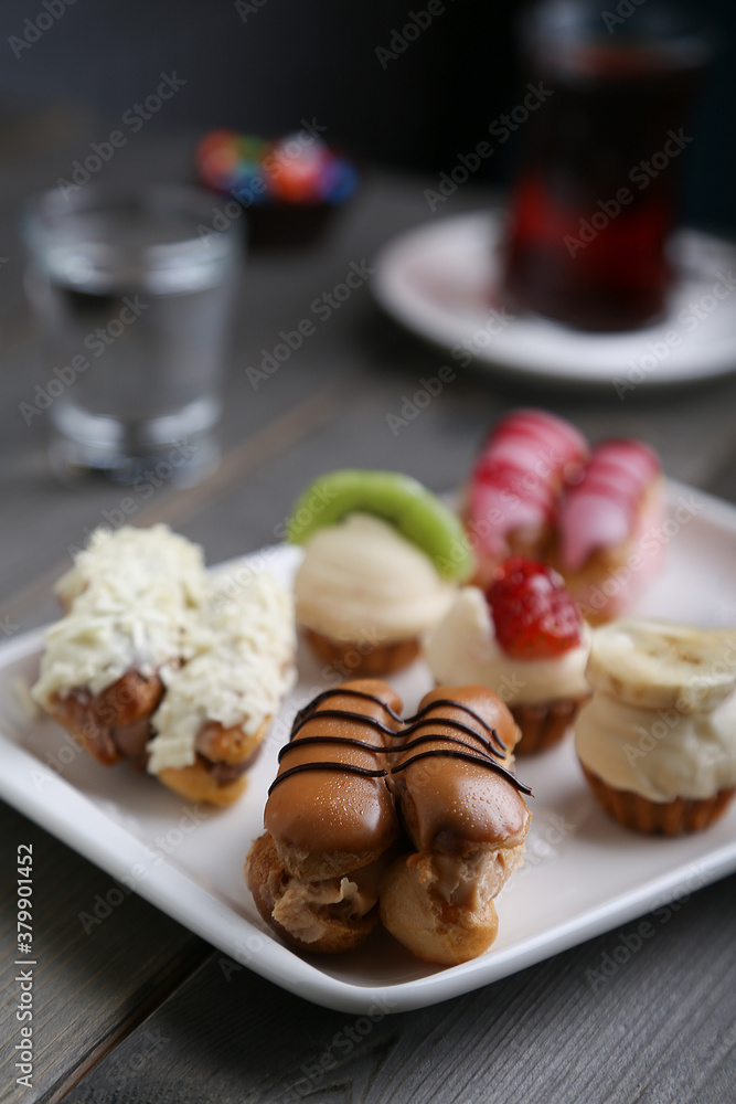 Eclairs and mini tarts on a white plate vertical view Eclairs and mini tarts on a white plate vertical view