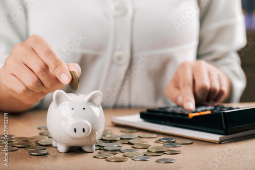 Vászonkép woman hand holding coins putting in piggy bank