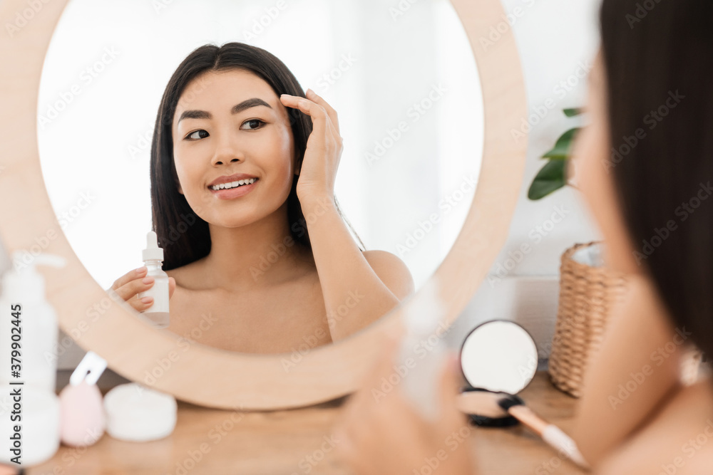 Smiling asian young woman applying facial serum Smiling asian young woman applying facial serum
