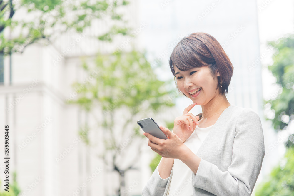 オフィス街でスマートフォンを操作する若い女性 オフィス街でスマートフォンを操作する若い女性