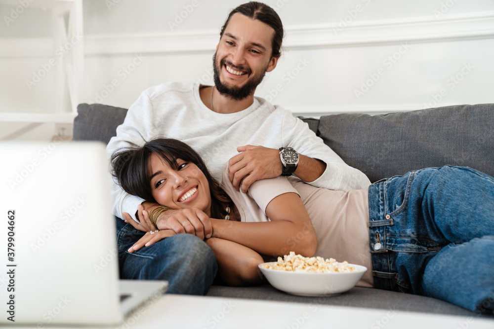 Image of cheerful couple watching movie on laptop and eating popcorn