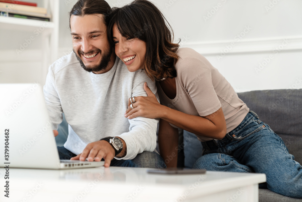 Image of cute cheerful couple using laptop and hugging Image of cute cheerful couple using laptop and hugging