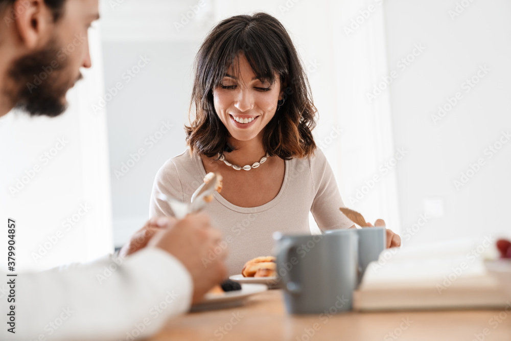 Image of smiling beautiful couple having breakfast while reading book Image of smiling beautiful couple having breakfast while reading book