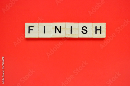 Word finish. Wooden blocks with lettering on top of red background. Top view of wooden blocks with letters on red surface