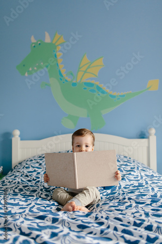 Cute young boy sitting on his bed reading a book photo