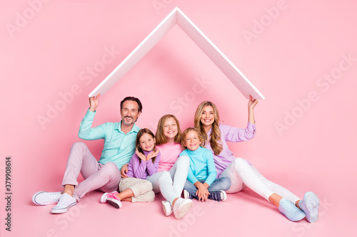 Full body photo of positive harmony family mommy daddy and three little preteen kids hold paper card roof sit floor dream about new apartment isolated over pastel color background © deagreez