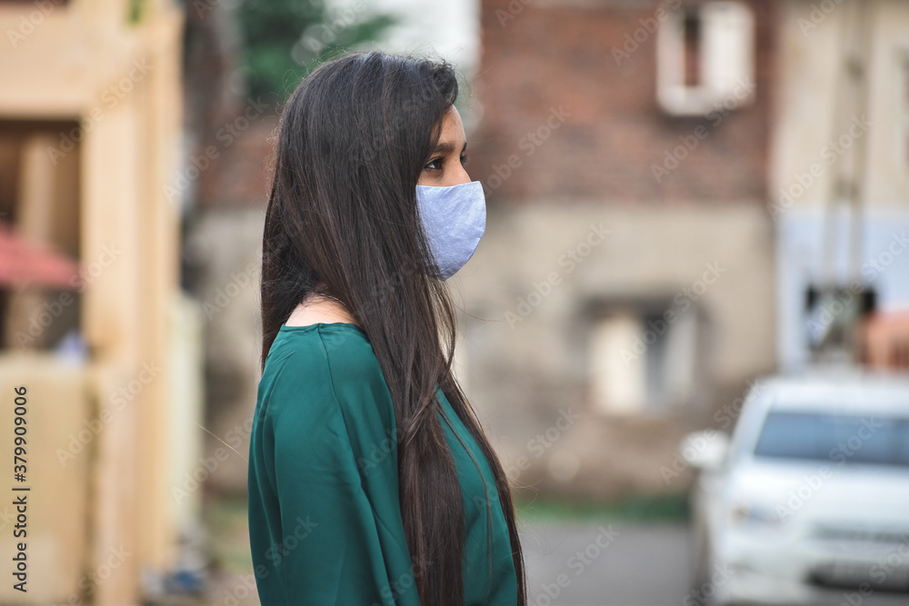 Fototapeta premium Portrait of an Indian female wearing medical mask to protect herself from corona virus pandemic while standing on street