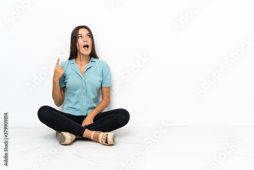 Teenager girl sitting on the floor pointing up and surprised