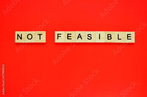 Word not feasible. Wooden blocks with lettering on top of red background. Top view of wooden blocks with letters on red surface