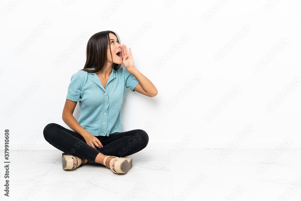 Teenager girl sitting on the floor shouting with mouth wide open to the lateral