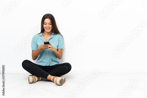 Teenager girl sitting on the floor sending a message with the mobile