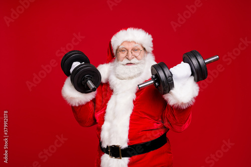 Portrait of his he nice handsome attractive cheerful cheery strong bearded Santa father wearing festal warm coat doing fit exercise isolated bright vivid shine vibrant red color background