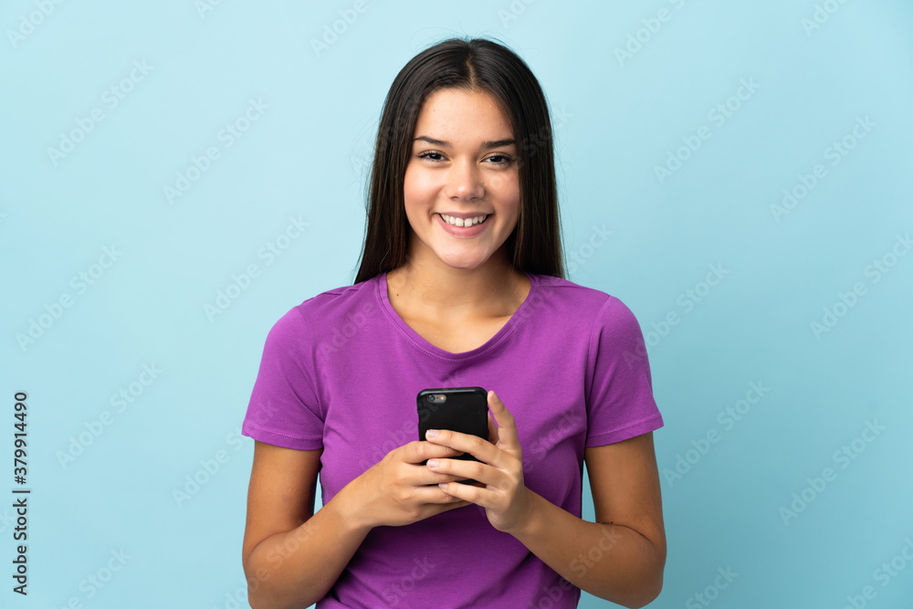 Teenager girl isolated on pink background looking at the camera and smiling while using the mobile Teenager girl isolated on pink background looking at the camera and smiling while using the mobile