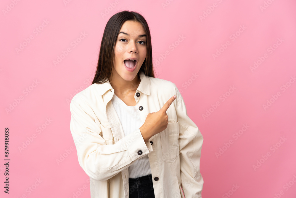 Teenager girl isolated on pink background surprised and pointing side Teenager girl isolated on pink background surprised and pointing side