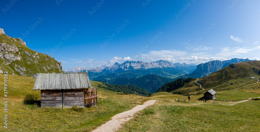 Hiking in the Dolomites - beautiful mountain panorama in the background and traditional huts in the foreground, South Tirol Italy