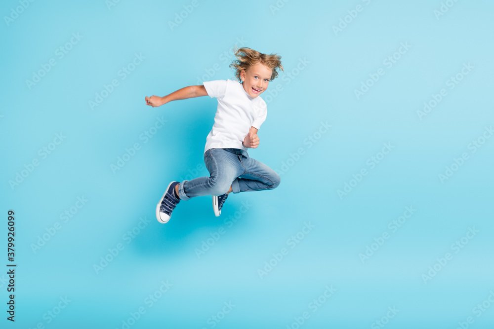 Little kid jump motion funny grimace hands wear white shirt jeans sneakers isolated blue color background