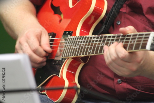 Nahaufnahme einer roten Jazzgitarre mit sich bewegenden Fingern des Musikers. Vollschlanker Musiker mit seinem fetten Instrument. Gitarre im close up mit Jazz auf den Seiten. Guitar Solo in action . photo