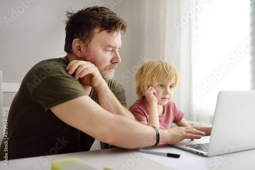 Father helping his schoolboy use the computer app for study using laptop in the home. Child and gadgets. Online education and distance learning for kids.