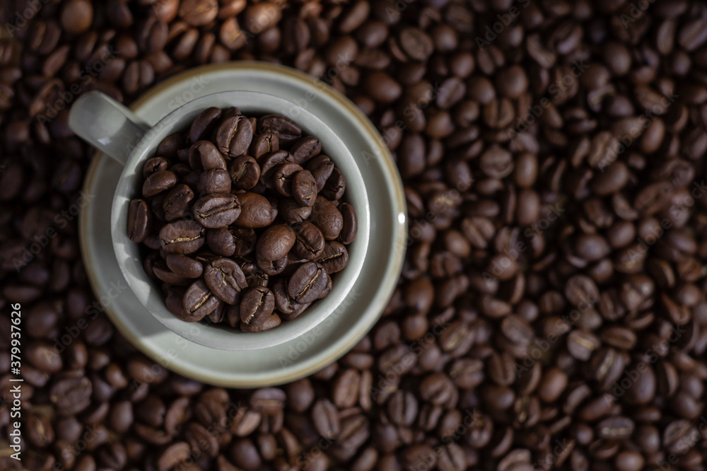 Coffee beans in light brown cup on the coffee beans background top view