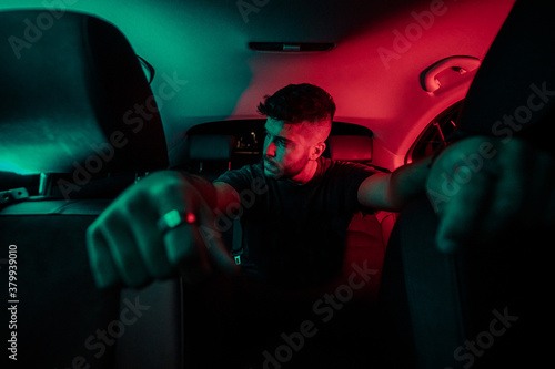 Chico joven de moda en un coche con luces de colore moderno 