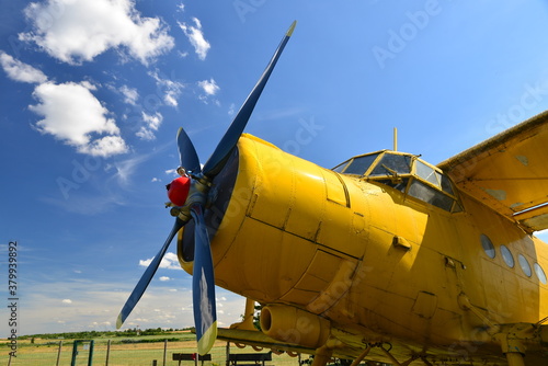 Close-up view of an old yellow plane. Isolated yellow bi plane on grassy meadow under blue sky with dynamic clouds. Aircraft at a grassy airfield.