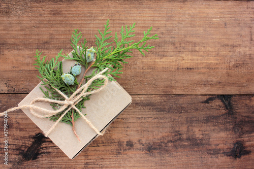 Christmas present on a wooden table. Brown craft gift box tied with rope and decorated with a evergreen twigs. Christmas background. Creative Flat lay, copy space. Rustic eco style