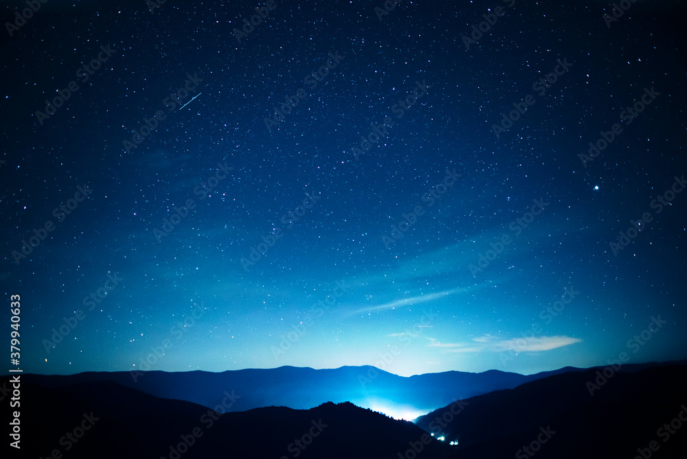 Starry sky over mountains panorama with city lights below