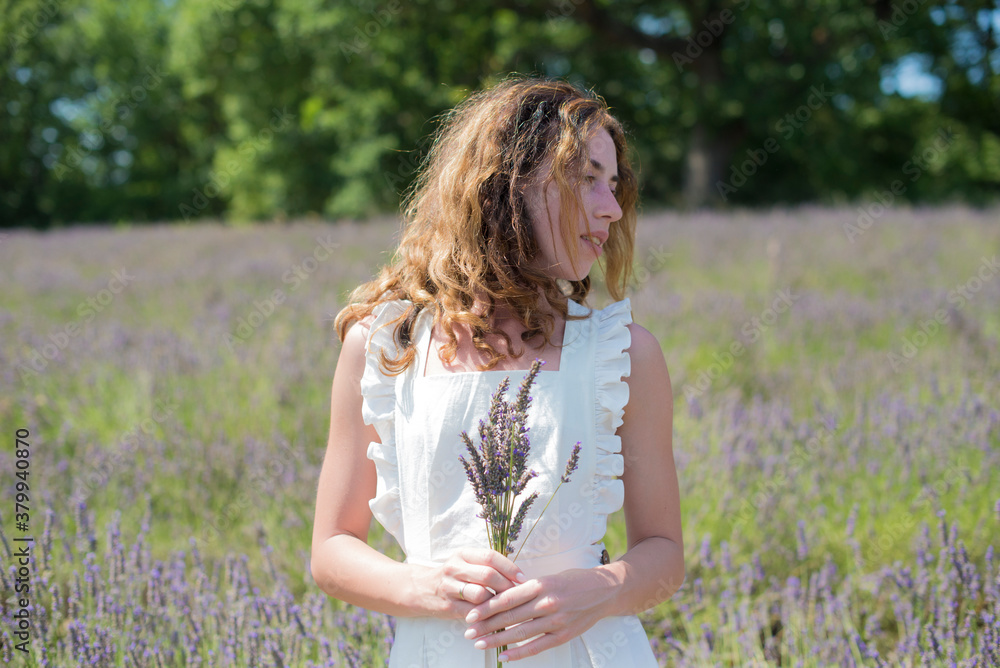 Fototapeta premium Brunette curly hair girl standing in the lavender field in France